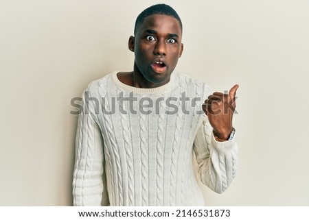 Young african american man wearing casual clothes surprised pointing with hand finger to the side, open mouth amazed expression. 