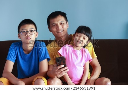 Portrait of a Thai family with father, son and daughter. It is a picture that feels full of love and warmth. sitting on the sofa in the house Father and mother take good care of their children.
