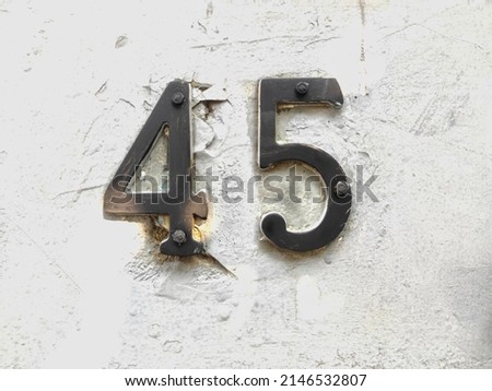 Black metal number 45 house number on white wall background. Forty-five digit. Close up