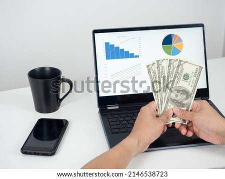 Man hand holding money dollar and using laptop on the table with mobile phone