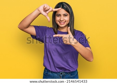 Young hispanic girl wearing casual purple t shirt smiling making frame with hands and fingers with happy face. creativity and photography concept. 