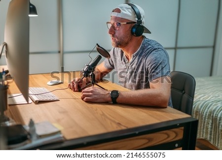 Middle-aged Blogger man in headphones reading text recording voice or making online webinar or news announcement. Modern home sound studio audio recording or live streaming technology concept.