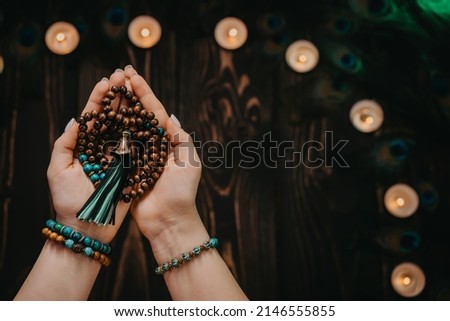 Woman holds in hand wooden mala beads strands used for keeping count during mantra meditations. Weaving and creation. Wooden background with candles and feathers. Spirituality, religion, God concept