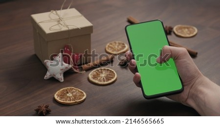 man hand use smartphone with green screen with christmas gifts and decorations on background