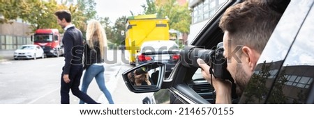 Private Detective Taking Photos Of Man And Woman On Street