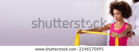 Physiotherapist Assisting Woman While Exercising With Exercise Band Royalty-Free Stock Photo #2146570495