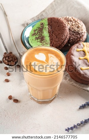 A glass of cappuccino or latte with foam and an artistic pattern. Coffee and cookies on the table for breakfast