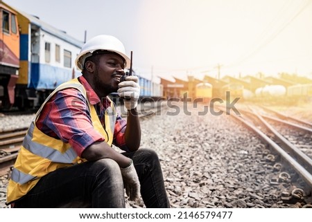 Portrait of handsome Africa American engineering using walkie talkie for control labor in front of train garage. Back view of contractor on background of outdoor old train garage