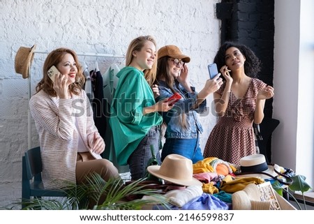 Young women talking on mobile phone, taking pictures, chatting on social networks at swap party. Casual clothes, shoes, hats, bags, jewellery. Eco friendly cloth concept. Reduce and reuse, donation