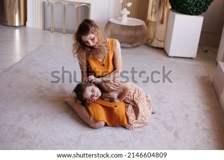 Portrait of lovely family mother and daughter embracing and kissing each other at home. Happy sweet woman with little 6-year-old girl in yellow dresses, family look, sitting on floor. Sweet family