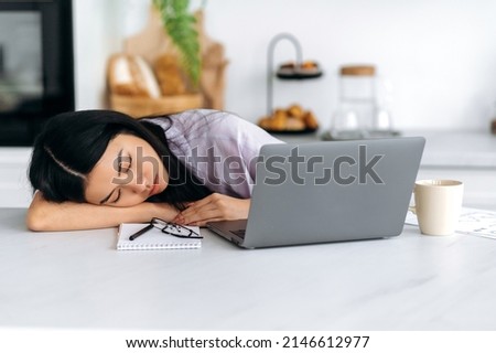 Fatigue concept. Tired exhausted Asian millennial girl, student or freelancer, fell asleep on the table while working remotely or studying in a laptop at home, is overworked, needs rest Royalty-Free Stock Photo #2146612977