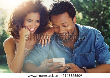 We both look good in this picture actually. Shot of an affectionate young couple using a cellphone together while relaxing outdoors.