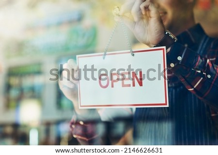 Opening day has arrived. Closeup shot of a young man hanging up an open sign in a shop window.