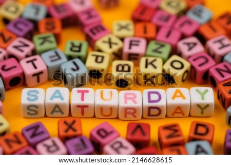 Saturday word on white colorful plastic block cube. Selective focus. Colorful dice on yellow background. 