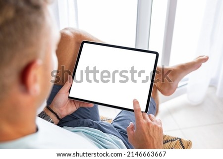 Man using tablet computer at home, blank white screen mockup