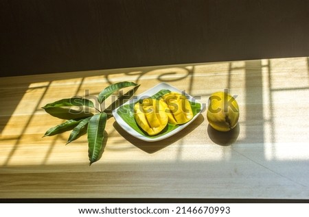 Ripe mangoes are placed on a plate on the table with a bouquet of leaves.