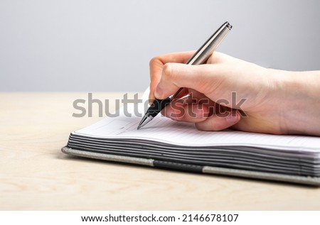 Woman hand closeup taking notes in planner. Female writing with pen information, reminders, schedule in diary. Handwriting. High quality photo