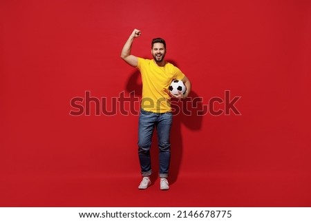 Full size body length happy young bearded man football fan in yellow t-shirt cheer up support favorite team hold soccer ball doing winner gesture isolated on plain dark red background studio portrait Royalty-Free Stock Photo #2146678775