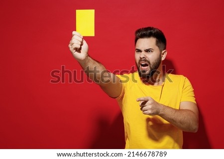 Angry young bearded man football trainer in t-shirt hold soccer ball point finger aside show yellow card isolated on plain dark red background studio portrait. People sport leisure lifestyle concept Royalty-Free Stock Photo #2146678789