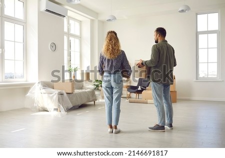 This is our home now. Young married couple settling down in new place. Rear view from behind of two people who are moving house or apartment standing in spacious room, holding boxes and looking around Royalty-Free Stock Photo #2146691817