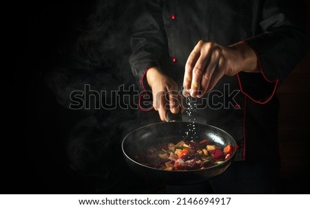 Cooking fresh vegetables. The chef adds salt to a steaming hot pan. The idea of European cuisine for a hotel with advertising space Royalty-Free Stock Photo #2146694917
