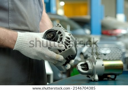 Spare parts. Elements of the electrical system of the car engine. The car generator is in the hands of an auto mechanic. There is a car starter on the desktop. Repair and maintenance of the car in the Royalty-Free Stock Photo #2146704385