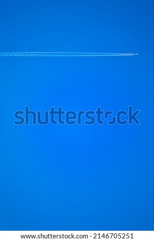 The plane, with a long inversion trail of smoke from the engines, against a background of deep blue sky. Bright colors, interesting geometry, abstraction.