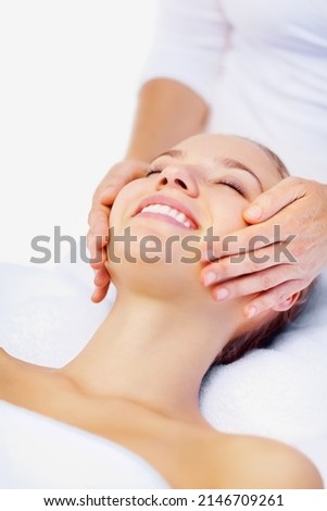 Happy female receiving a facial massage from a masseuse. Smiling young woman enjoying a massage while at a dayspa.