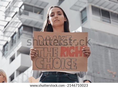 Make the right choice for you. Cropped portrait of an attractive young woman holding up a sign protesting against the covid 19 vaccine with other demonstrators in the background.