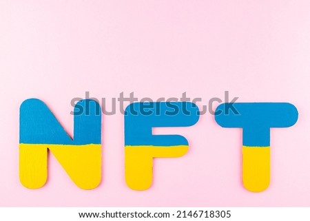 NFT (Non-Fungible Token) in Ukrainian flag colors. Blue-yellow NFT inscription on pink background. Ukraine support concept. Top view. Copy space
