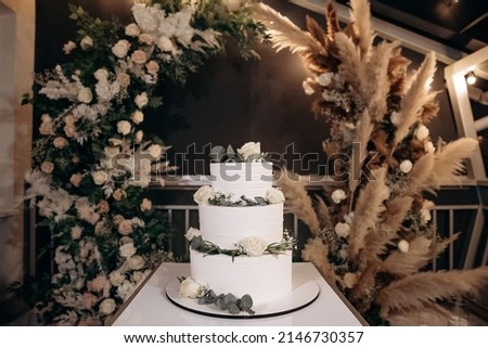 Large luxury wedding cake on a background of a flowering arch in the style of boho. Wedding dessert under the light of evening light bulbs. Wedding decor. Royalty-Free Stock Photo #2146730357