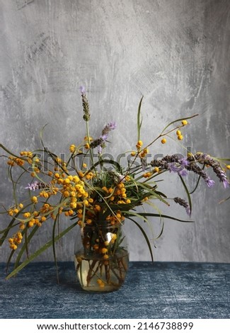 Spring flowers in a glass jar. Simple composition still life with acacia and lavender flowers. Light grey background with copy space. 