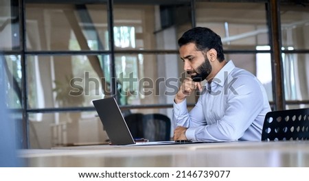 Thoughtful concentrated indian business man entrepreneur investor manager using computer, watching webinar working in office analyzing online data market thinking doing web research looking at laptop. Royalty-Free Stock Photo #2146739077