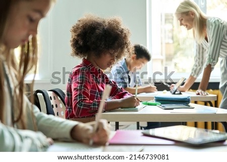 Diligent concentrated hard working diverse miltiethnic classmates schoolchildren writing tasks in notebooks with happy teacher explaining and helping. Schoolwork in diversity team. Education concept. Royalty-Free Stock Photo #2146739081
