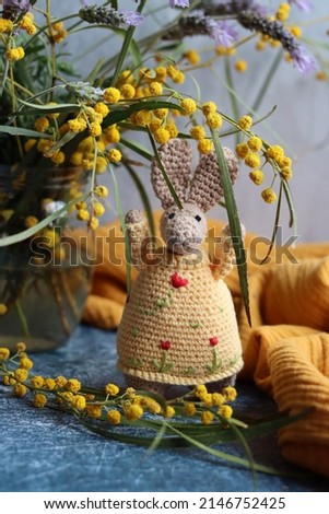 Crochet Easter bunny on grey background. Beautiful spring bouquet of mimosa and lavender flowers on a table. Hobbies and free time concept.  