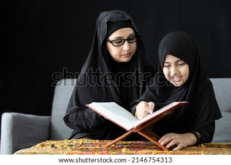 muslim mother with her daughter reading a holy book or Quran on sofa and black background
