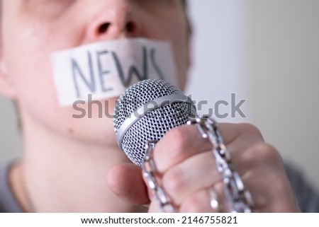 A man gags his mouth with duct tape saying news trying to speak into a microphone. The concept of World Press Freedom Day. Royalty-Free Stock Photo #2146755821