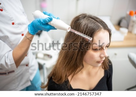 Professional beautician doing darsonval hair treatment procedure for young woman in beauty salon. High quality photo