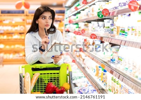 Arabic Woman With Shopping List Writing Calculating Prices Buying Groceries In Supermarket On Weekend. Financial Crisis And Household, Finances And Family Budget