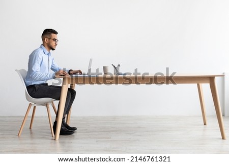 Profile Side View Portrait Of Focused Middle Eastern Male Manager In Glasses Working On Laptop Computer In Modern Office, Serious Guy Sitting At Desk And Using Pc, Looking At Screen Watching Webinar Royalty-Free Stock Photo #2146761321