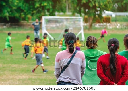 Back view of Moms watch and cheering their sons playing football in school tournament on sideline. Sport, outdoor active,  Spectator watching soccer game. Parents care and encourage their children. Royalty-Free Stock Photo #2146781605