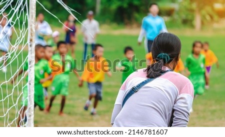 Back view of Mom watch and cheering her son playing football in school tournament on sideline. Sport, outdoor active,  Spectator watching soccer game. Parents care and encourage their children. Royalty-Free Stock Photo #2146781607