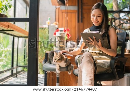 asian adult female creative designer casual relax working with her cat pet morning weekend at home studio,young asian asian wear apron research information for her workshop via tablet device