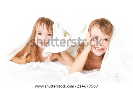 happy little girls twins sister in bed under the blanket having fun, smiling
