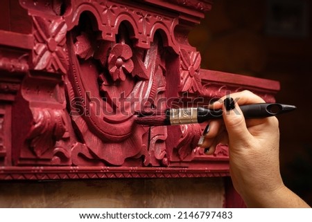 Woman finishing to patinate wooden antique cupboard ornaments in pink color with big paint brush. Giving new life to old stuff. Hand restoration of old furniture.