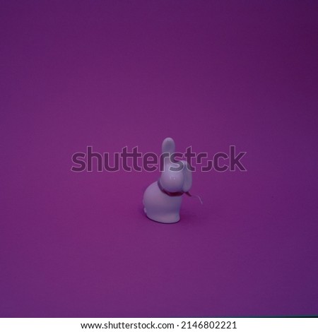 Ceramic figurine of a  rabbit with a decorative ribbon on a purple  background. Flat lay concept.