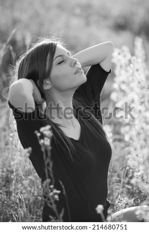 Black and white photo of beautiful girl with long, straight hair posing in the field looking melancholic 