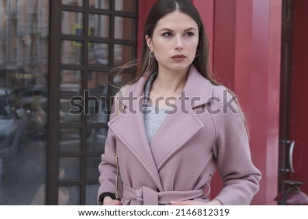 a beautiful girl in a pink coat on the street near a red building