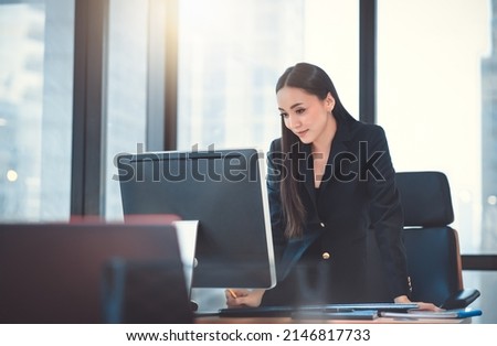 Young adult smart asian business woman in black casual suit using laptop working overtime in urban office.