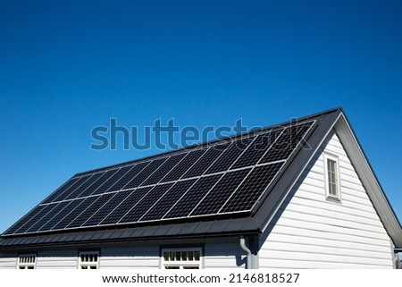 Solar panels on small wood board domestic house roof, sustainable energy concept. Lot of copy space on clear blue sky. Royalty-Free Stock Photo #2146818527